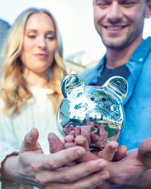Couple holding a piggy bank in front of a house
